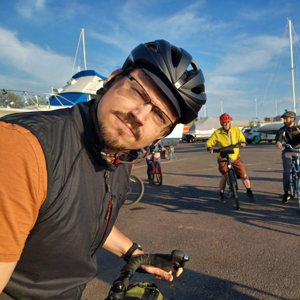 Man in bicycle helmet photo bombing a group of cyclists posing for a picture.