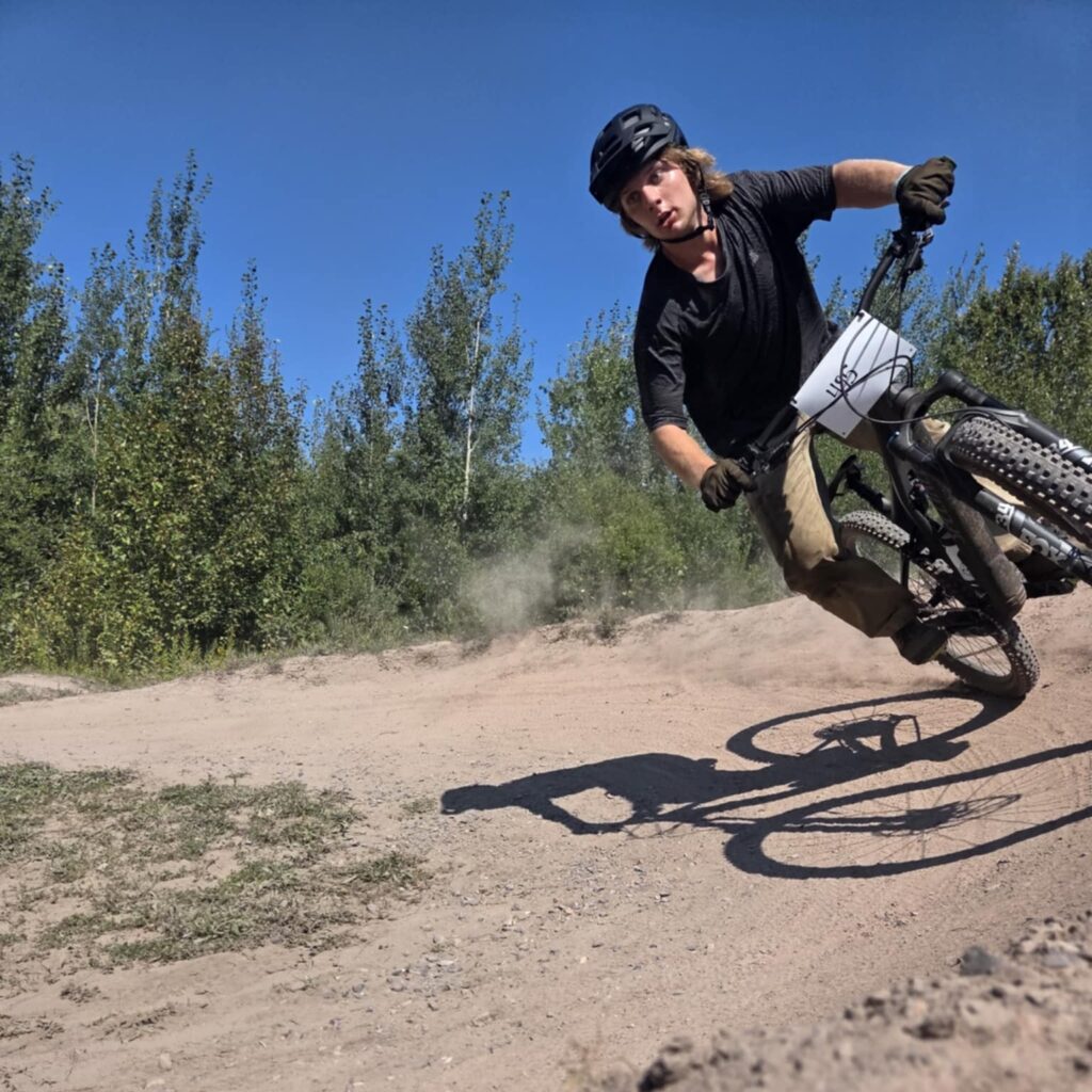 Young man mountain biking around a berm on an enduro bike with race tag.